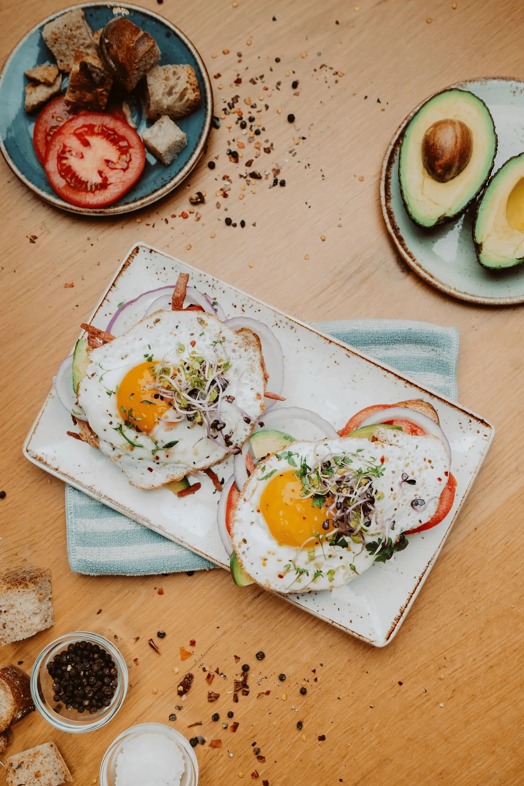 Spiegeleier mit Kresse auf einer Platte, daneben Avocado und Tomate